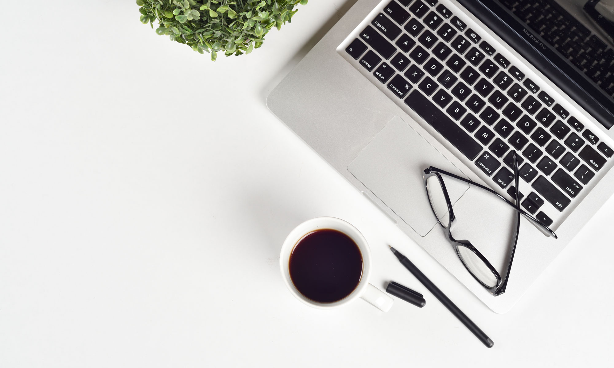 A laptop on a desk with glasses and a coffee cup