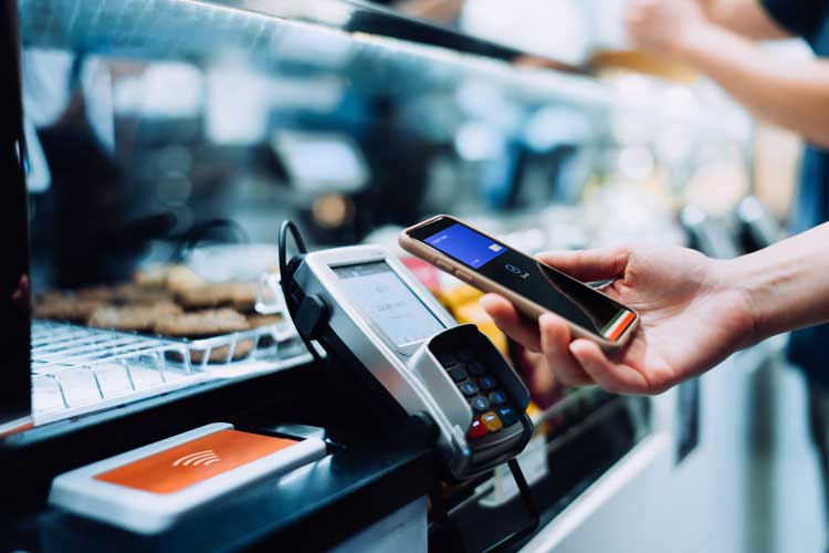 Close up of a woman's hand paying with her smartphone in a cafe, scan and pay a bill on a card machine making a quick and easy contactless payment. NFC technology, tap and go concept